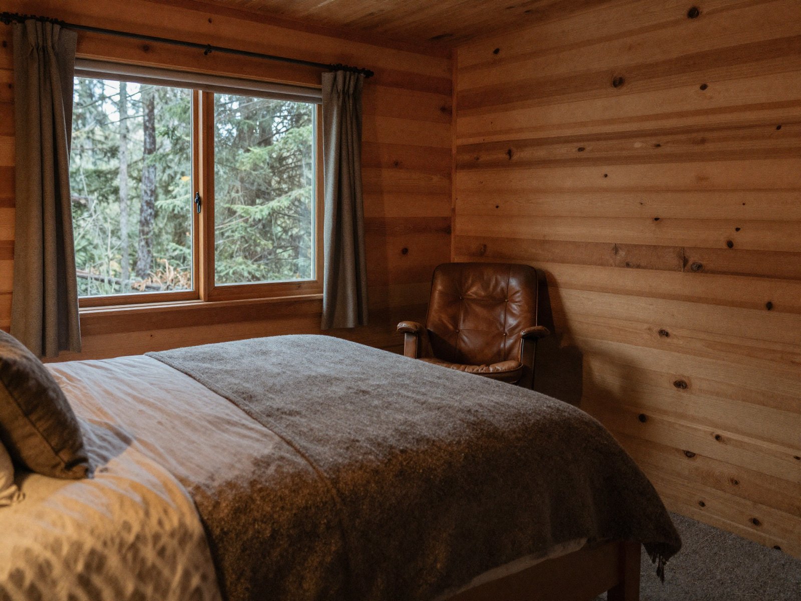 A cozy Lodge Room with a queen bed, fir-paneled walls, and a reading chair by the window